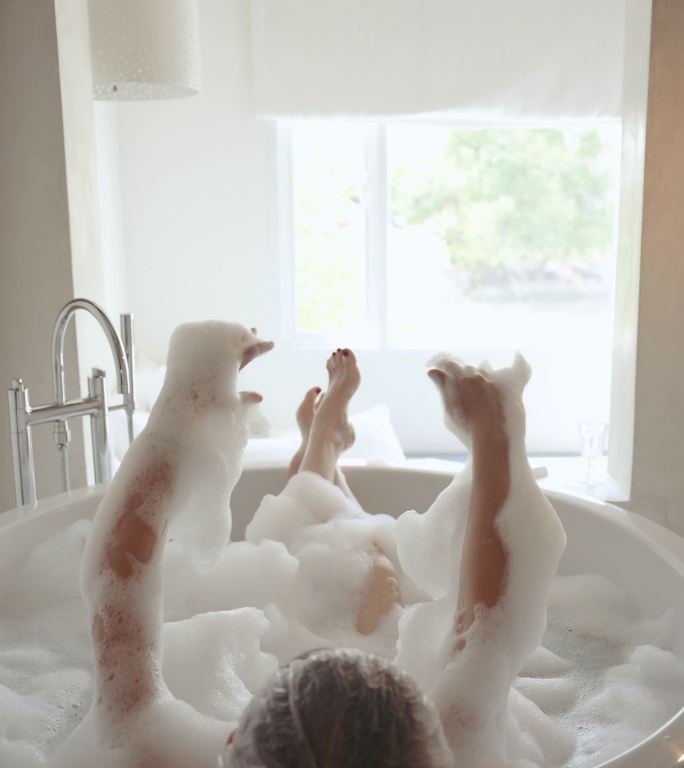年轻漂亮的女人躺在浴室里，手里拿着泡沫，玩着泡沫和泡泡