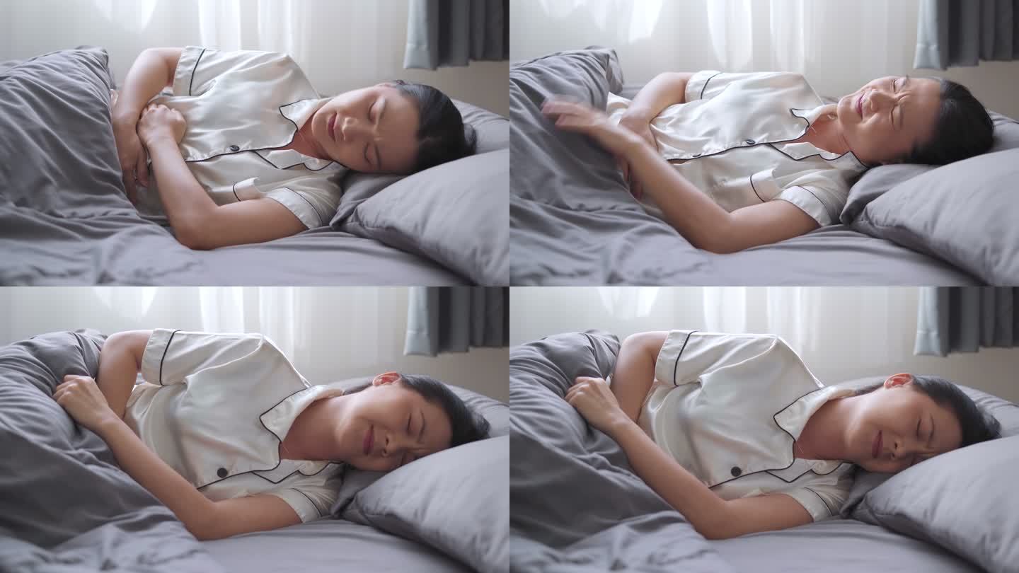 早上躺在床上的一位亚洲妇女胃痛。