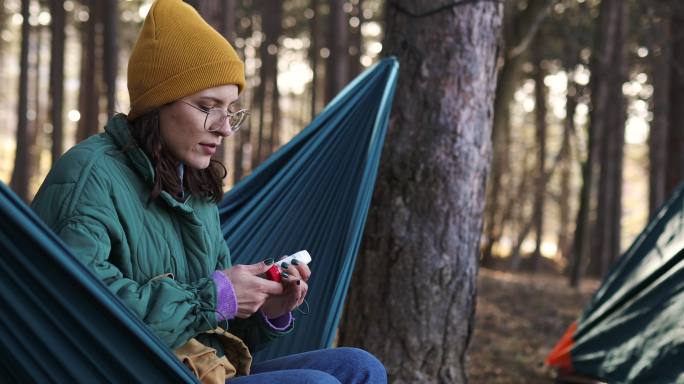 在一个阳光明媚、刮风的日子里，登山运动员在山上露营。她使用哮喘吸入器，因为她有呼吸问题