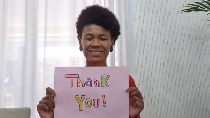 在视频通话中展示写有“谢谢”的纸的女人-网络摄像头视角