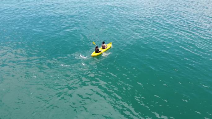 缩小镜头，看一对在海洋中划黄色皮艇的夫妇