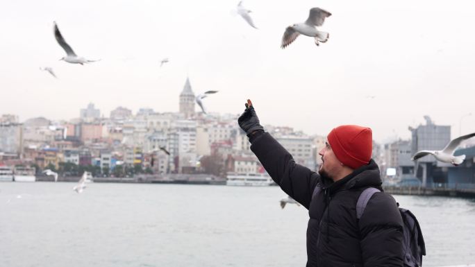 年轻人正在喂海鸥，海滩上刮起了暴风雨，年轻人正在伊斯坦布尔博斯普鲁斯海峡喂食海鸥