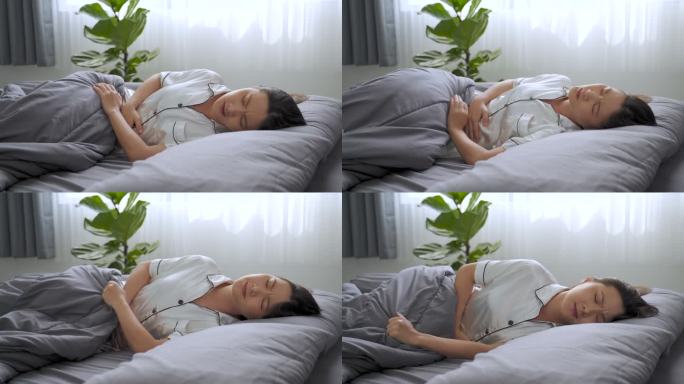 早上躺在床上的一位亚洲妇女胃痛。