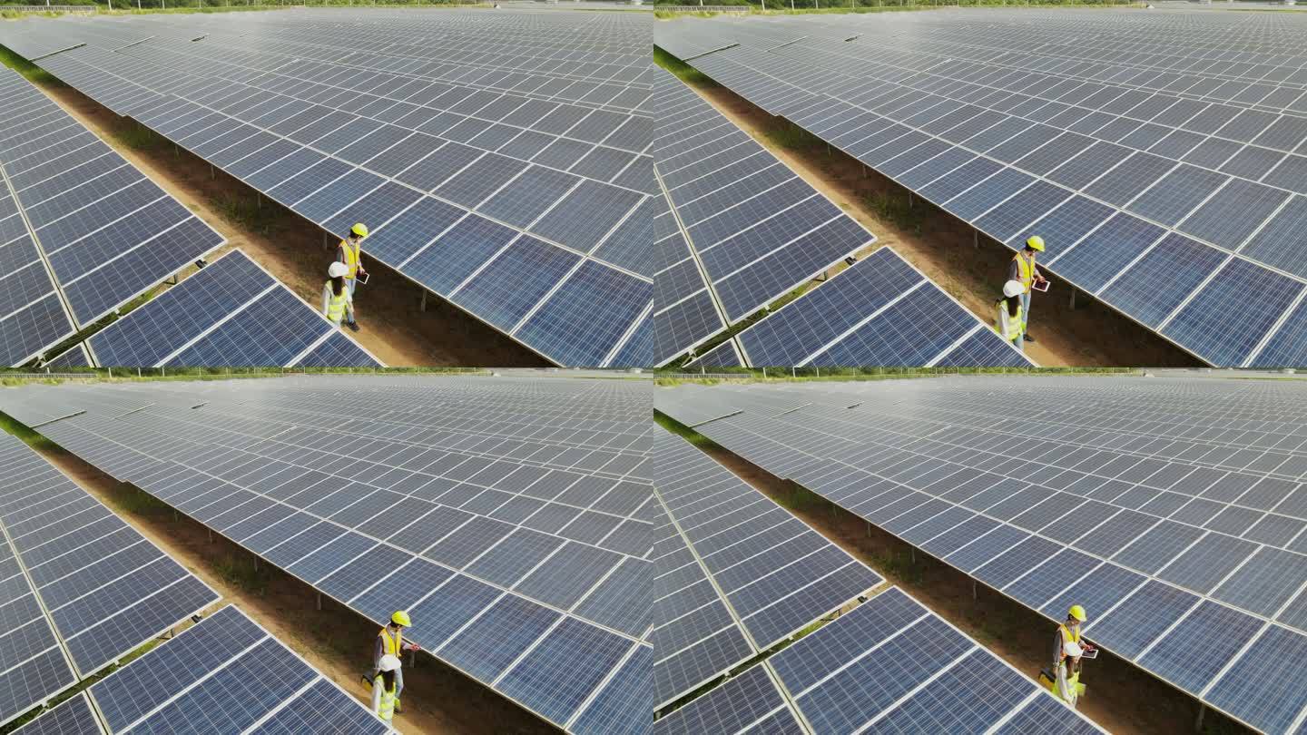 鸟瞰技术工程师穿过太阳能电池板，检查太阳能农场的太阳能电池板。