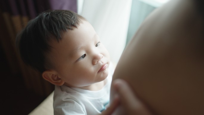 男孩在卧室里和怀孕的妈妈肚皮玩耍和接吻