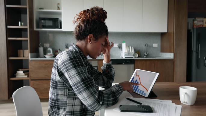在家工作的非裔美国女性担心经济衰退，并看着平板电脑上的图表