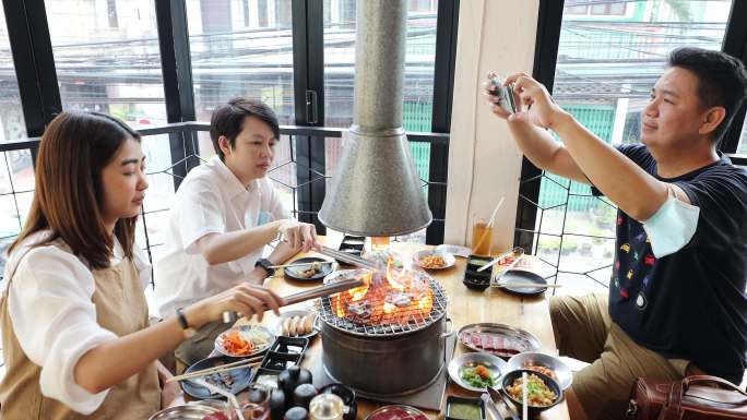 亚洲成人朋友在烧烤餐厅用智能手机拍照和视频点播