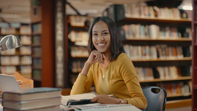快乐微笑的女学生在校园图书馆学习。年轻女性专注于为课程撰写论文。模块学期论文到期。专注于学位的文学、