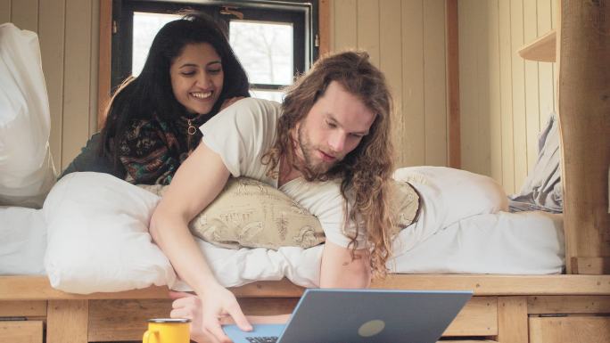 年轻夫妇在小房子度假租赁床上使用笔记本电脑