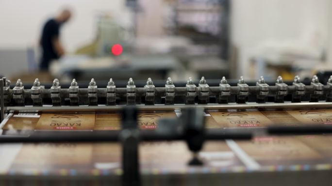 一台自动化机器的特写镜头，工人在后台工作时，将打印介质堆放在印刷厂