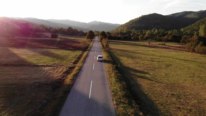 一辆灰色的汽车沿着一条空旷的乡村道路行驶。