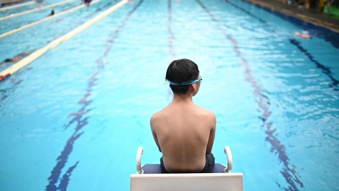 慢动作后视亚裔中国少年坐在游泳池边看