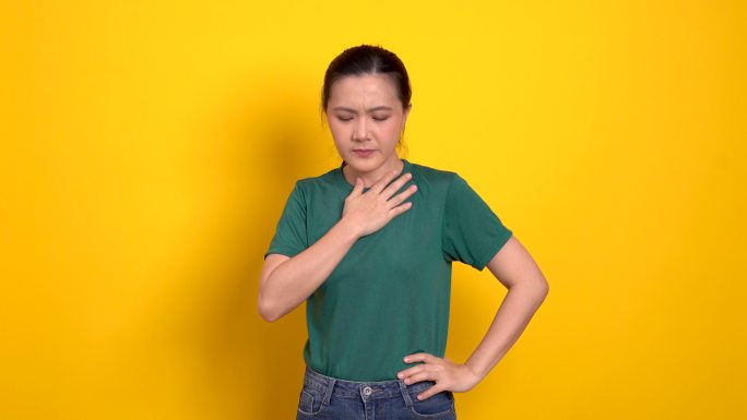 一名亚洲妇女因喉咙痛而生病，她被隔离站在黄色背景上。