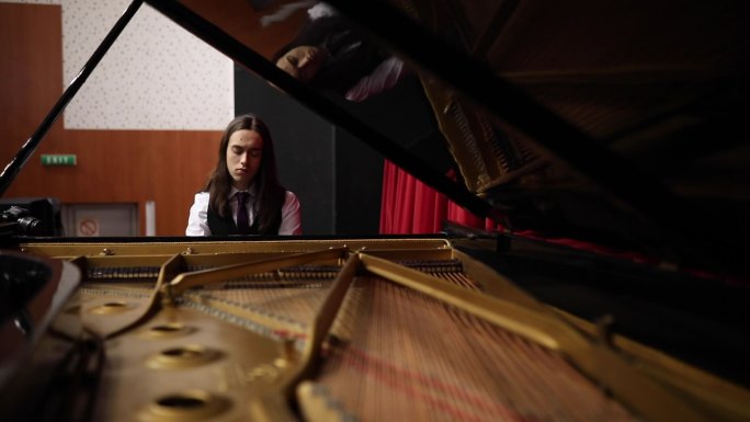 一位身穿燕尾服的天才年轻钢琴家在大钢琴上练习奏鸣曲。