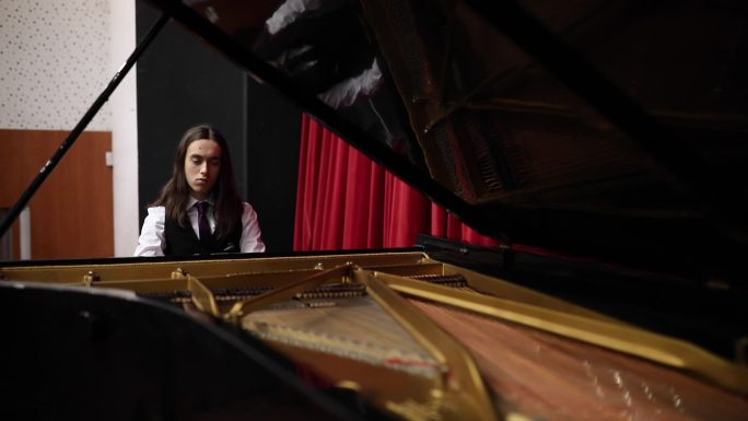 一位身着燕尾服、头发蓬松的钢琴家在大钢琴上练习奏鸣曲演奏。
