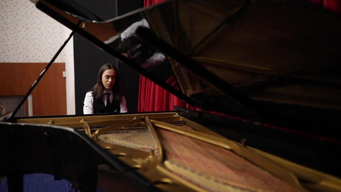 一位专心致志的年轻钢琴家在剧院里用大钢琴演奏乐曲。