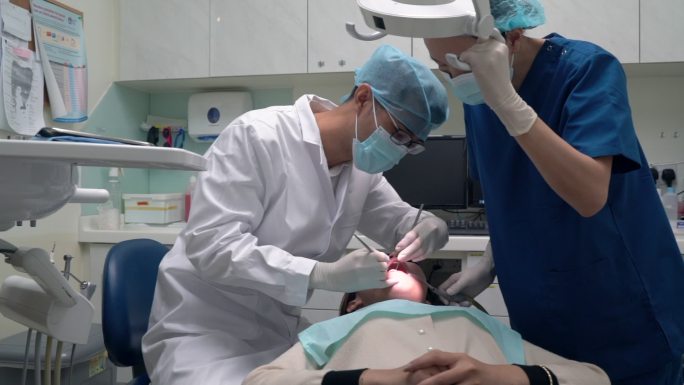 牙科护理-亚洲牙医在牙科助理在场的情况下检查患者时中途更换工具