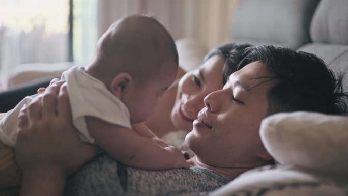 周末早上，亚裔中国父母在床上与男婴躺在一起