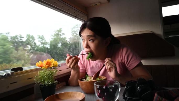 年轻的亚洲女性在面包车里享用沙拉早餐，从面包车侧窗向外看。
