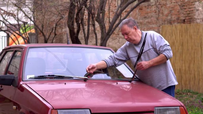 一位老人手里拿着水管，在后院洗车。