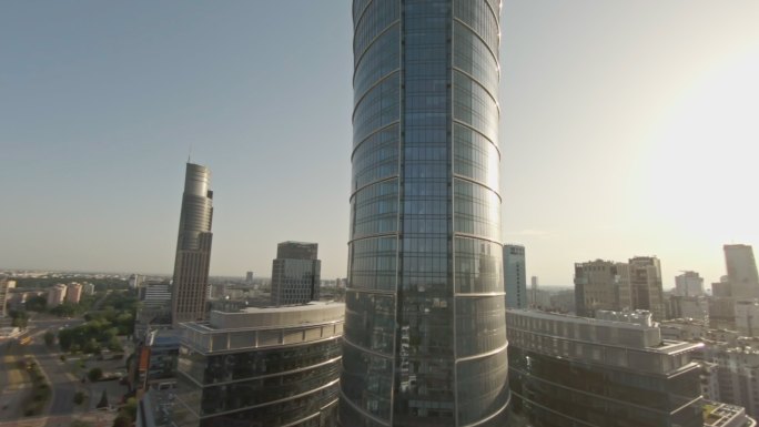 反射蓝天的玻璃摩天大楼。FPV无人机向下移动并远离建筑物