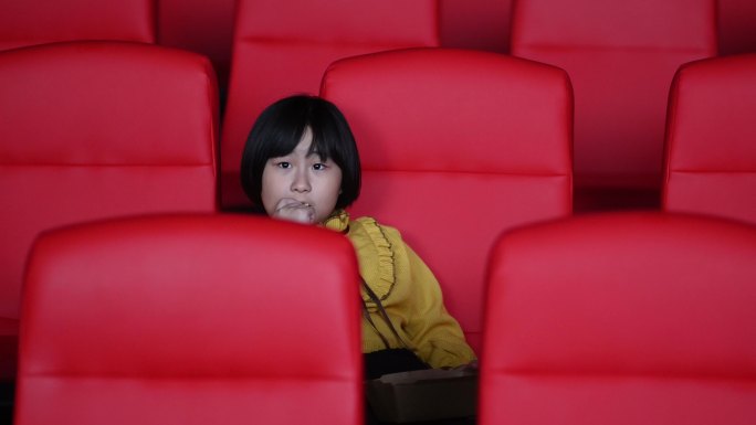 正视亚洲中国年轻女孩一边吃薯条一边独自在电影院看电影