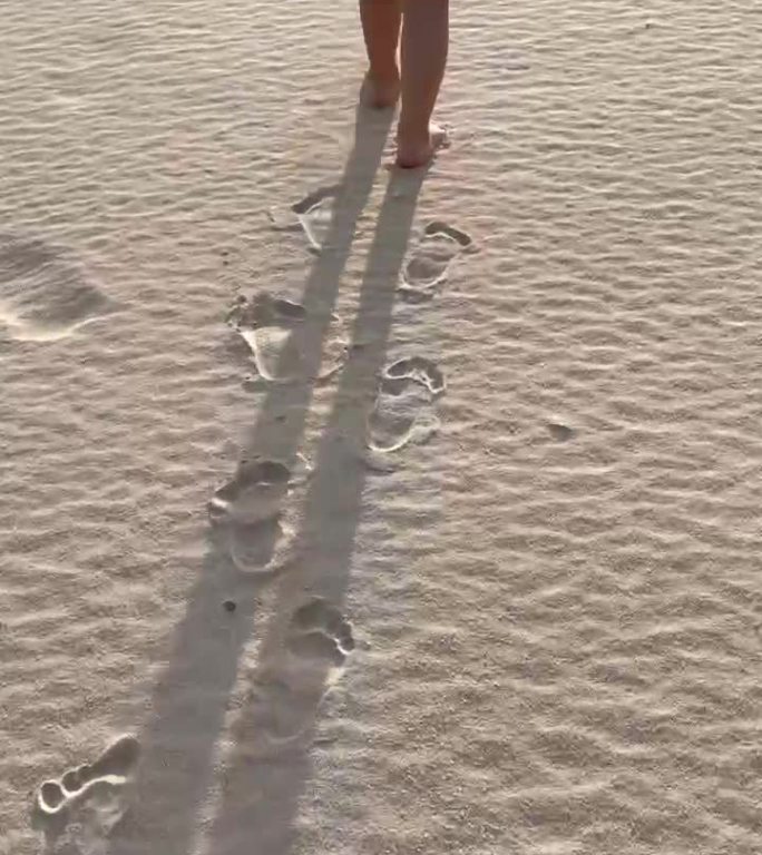 沙滩上一个赤脚的可爱小孩一步一个脚印走着