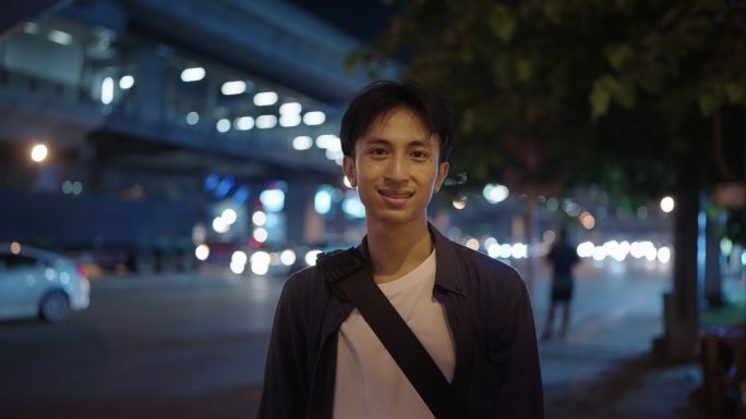 这是一张快乐的亚洲年轻人的脸，他晚上在城市里微笑。