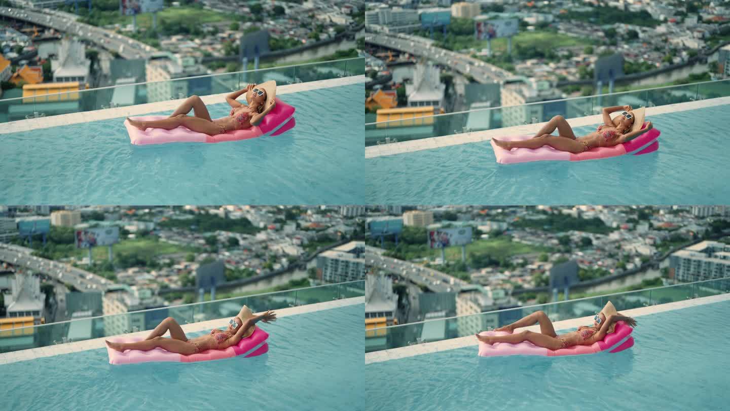 穿着比基尼的微笑女子躺在游泳池的气垫筏上晒太阳