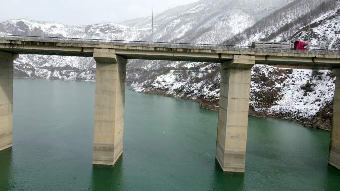 冬季飞车在冰河上过桥，桥梁和雪山的空中拍摄，两座雪山之间的桥梁连接，空中雪景，桥上的红色卡车，下雪天