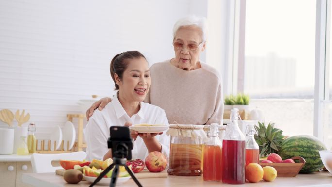 亚洲大女儿和母亲作为影响力人物，教授如何用不同的调味品制作自制发酵生红茶菌茶。健康的天然益生菌口味饮