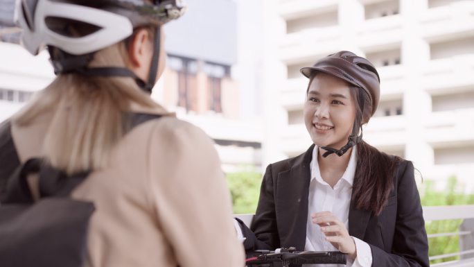 从肩上看，这位年轻的亚洲女商人戴着头盔，背着商务背包，与骑着电动踏板车上班的漂亮年轻同事会面。他们在