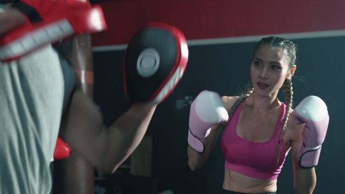 在健身房与大块头教练一起上拳击课的亚洲年轻女子。