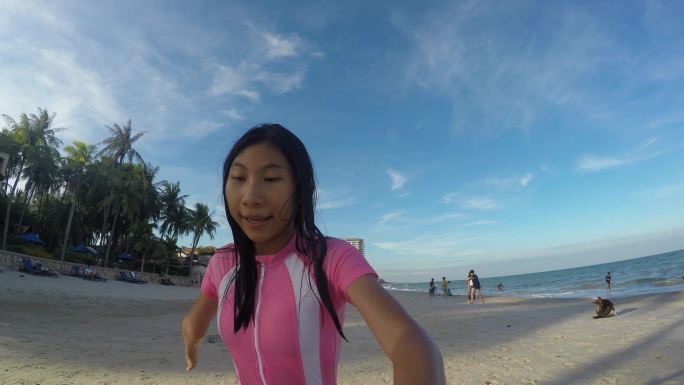 一个快乐的亚洲女孩穿着粉色泳衣在海滩上跑步，自拍自拍，参加vlog或博客等新生代活动。