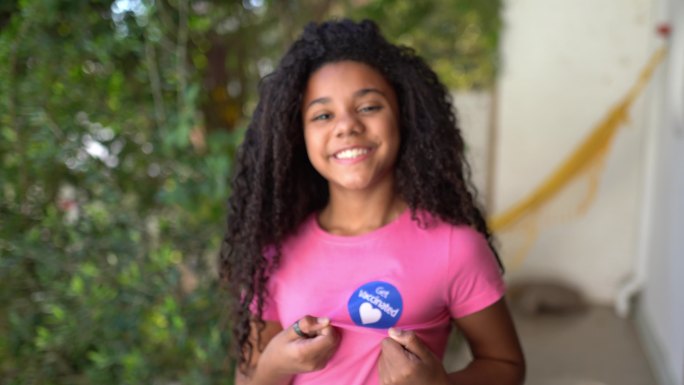 一个女孩的肖像，她的衬衫上贴着“接种疫苗”的标签