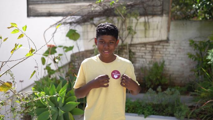 一个十几岁男孩的肖像，他的衬衫上贴有“接种疫苗”的标签