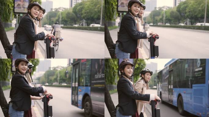 两名身着西装、头戴头盔的亚洲女商人站着，拖着她们的汽车、电动踏板车和自行车，等待穿越人行横道。一位女