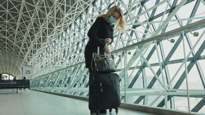 戴着医用口罩的女士带着行李在机场休息室散步