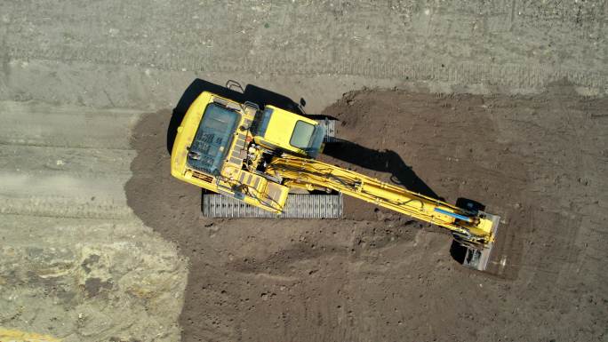 带有连续履带的黄色挖掘机。鸟瞰图。低空接近摄像机。整地挖掘机。施工现场准备。加注铲斗和驾驶室旋转。