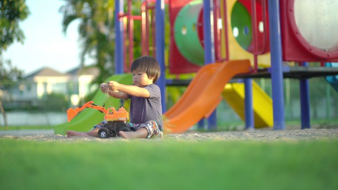 小男孩独自在操场上玩挖掘机玩具玩沙子