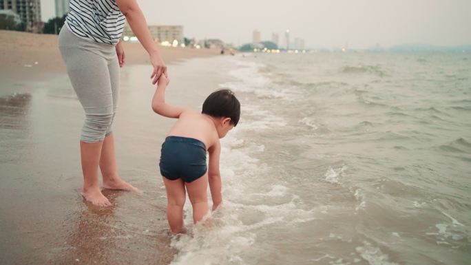 母亲手牵着手，小儿子在芭堤雅海滩上玩耍。