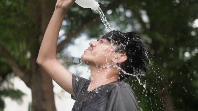 一名年轻的亚洲男子赛跑运动员在户外将水浇在头上
