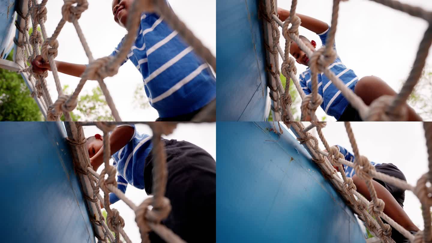 非洲黑人儿童，一名7岁男孩在儿童游乐场公园爬绳梯或网。男孩在障碍赛道上攀爬户外绳架
