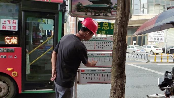 一位农民工在街道上搭公共汽车看线路路牌