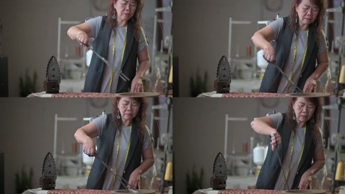 亚裔中国高级女裁缝用服务钳子从陶工手中拿起烧得滚烫的木炭，将其放入古董铁传统熨烫中