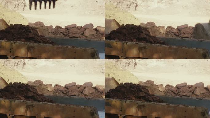 阳光明媚的施工现场，挖掘机铲斗将泥土和岩石倒入自卸车后部的特写镜头（铰接式自卸车）