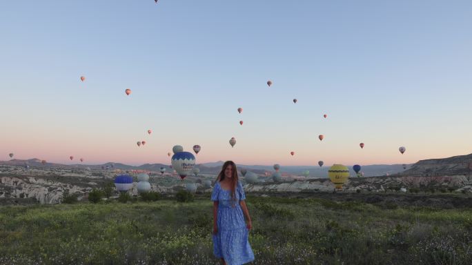 在卡帕多西亚，穿着裙子的快乐女人在风景秀丽的山谷中，手持热气球迎接日出