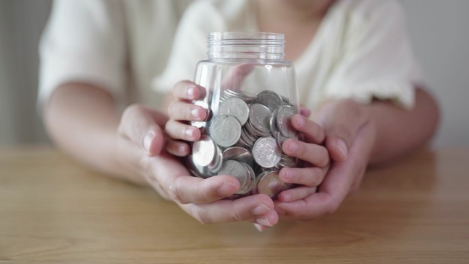 成人和儿童手拿一个装有硬币的罐子，慈善理念