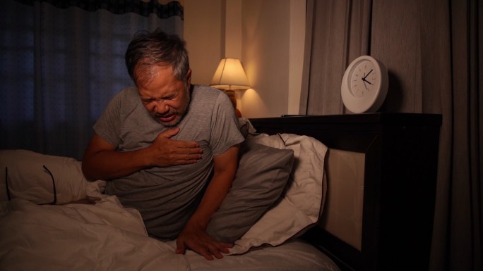 晚上躺在床上胸痛的亚洲男人。老人在床上心脏病发作。