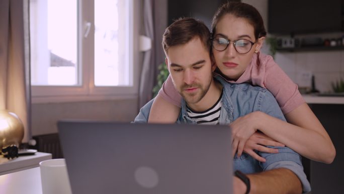 当男人在家工作时，爱她的年轻女人拥抱着他